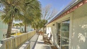 A covered outdoor deck with wooden furniture, palm trees, and a building with large windows. - Large Deck/ in-law suite /Walk to Beach/ Location! (Panama City Beach)