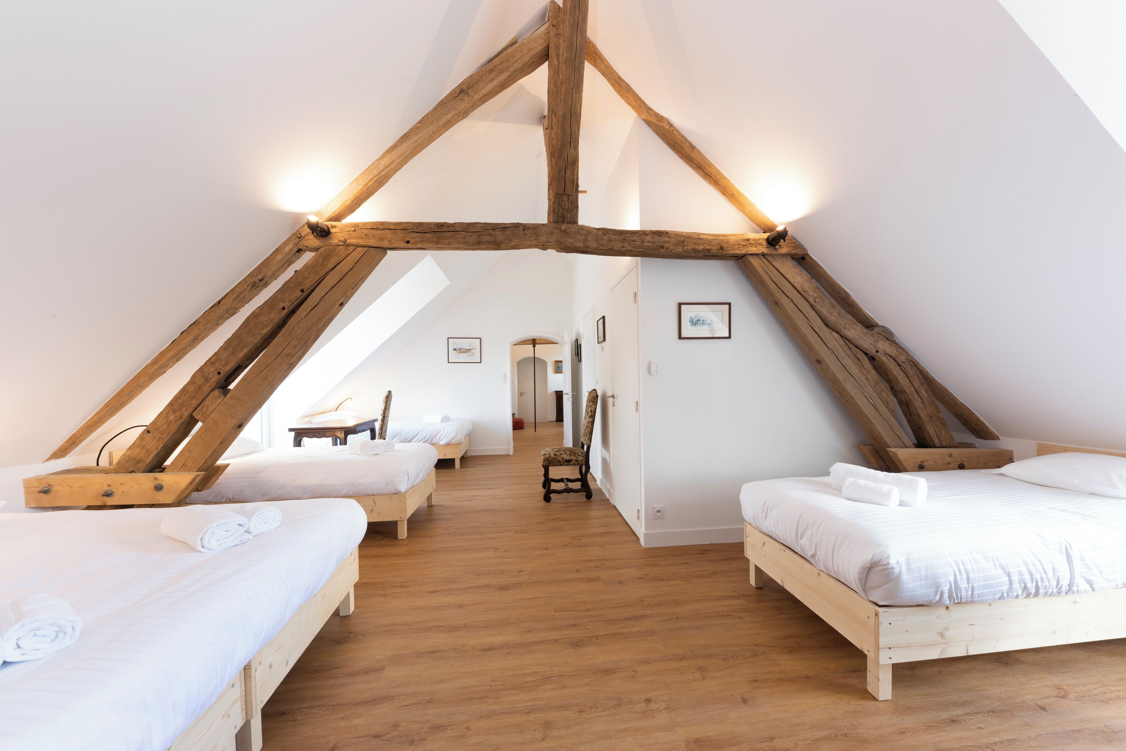 A bedroom with two beds, wooden beams, and a skylight.