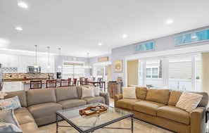 Un salon spacieux avec un canapé d’angle beige, une table basse en verre et un coin repas comprenant des chaises en bois et une table blanche.