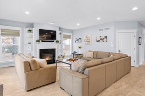 Un salon moderne avec une cheminée, des canapés de couleur beige, un téléviseur à écran plat et des œuvres d’art décoratives accrochées au mur.