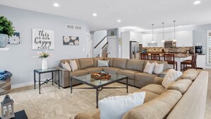 A modern living room with a sectional sofa, a glass coffee table, and a kitchen in the background. - 5 Bed on Cul-de-sac Downtown. Playground, Kayak Launch, Bike trails 1/2 block aw (Rehoboth Beach)
