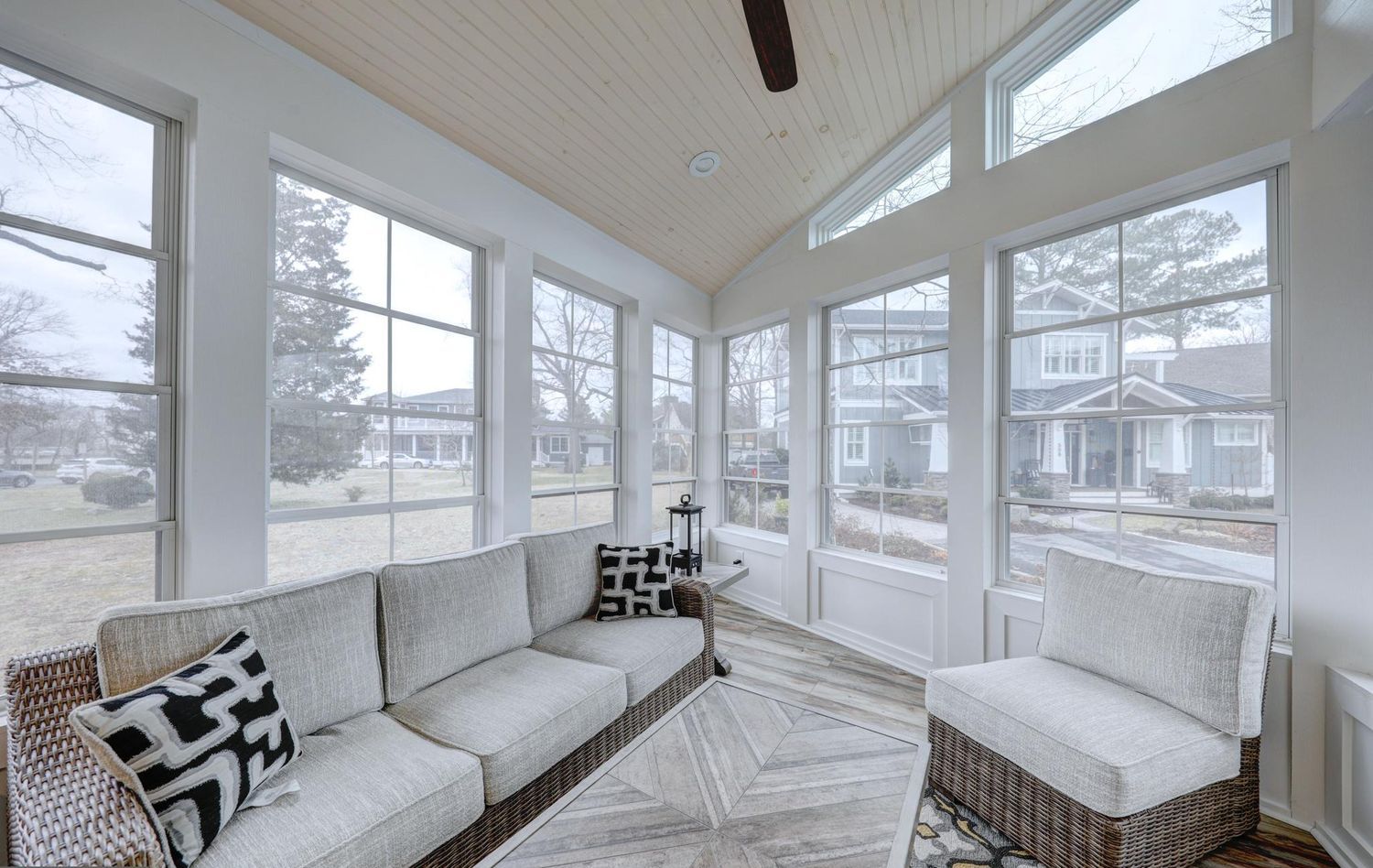 A sunroom with large windows, a sofa, a chair, and a patterned rug.