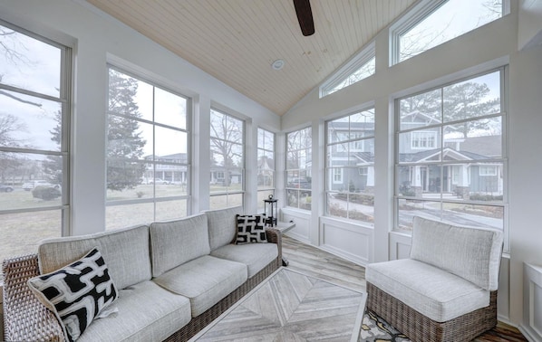 A sunroom with large windows, a sofa, a chair, and a patterned rug.