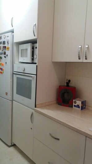 Eine Küche mit Kühlschrank, Mikrowelle, Backofen und einem roten Gerät auf der Arbeitsfläche.