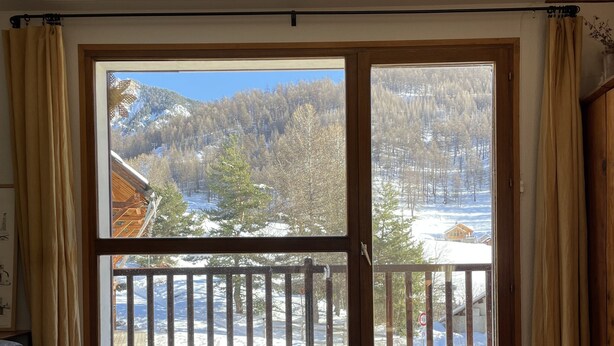 A room with a large sliding glass door leading to a balcony with a view of a snowy mountain landscape. - Spacious, comfortable apartment at the foot of the slopes (Arvieux)