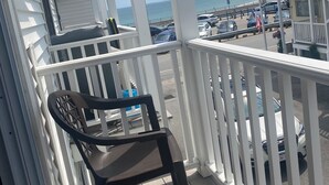 A balcony with a view of the beach and parked cars.