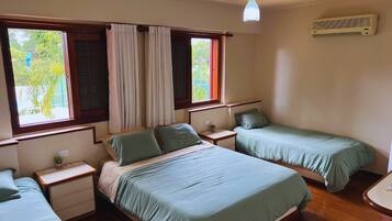 A bedroom with two single beds, a ceiling fan, an air conditioning unit, and a window with curtains.