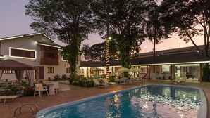 Una piscina con sillas de descanso y sombrillas, rodeada por un edificio con techo de tejas y un jardín.