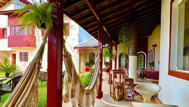 Un espacio al aire libre techado con hamacas, una mesa blanca y un estante decorativo.
