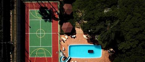 Vista aérea de una propiedad con cancha de baloncesto, piscina y mobiliario exterior.