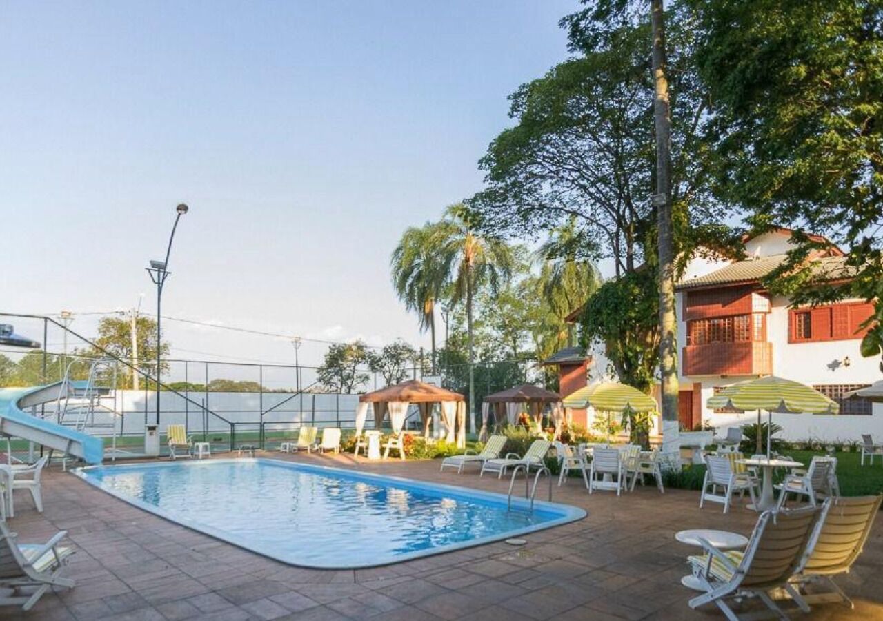 Une piscine entourée d’une clôture et d’arbres, avec des chaises longues et des parasols.