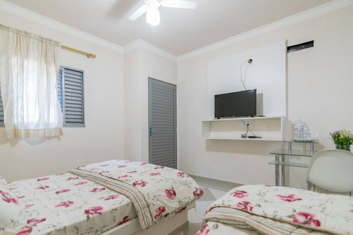 A bedroom with two beds, a TV, a desk, and a chair.
