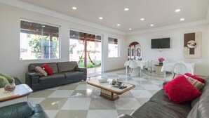 Un salón amplio con suelo a cuadros, un sofá gris, una mesa de centro y una zona de comedor con una mesa y sillas blancas.