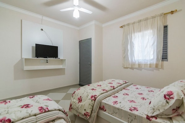 A bedroom with two single beds, a ceiling fan, a TV on a shelf, a window with curtains, and a door. - The Helvetia Polo Villa (Indaiatuba)
