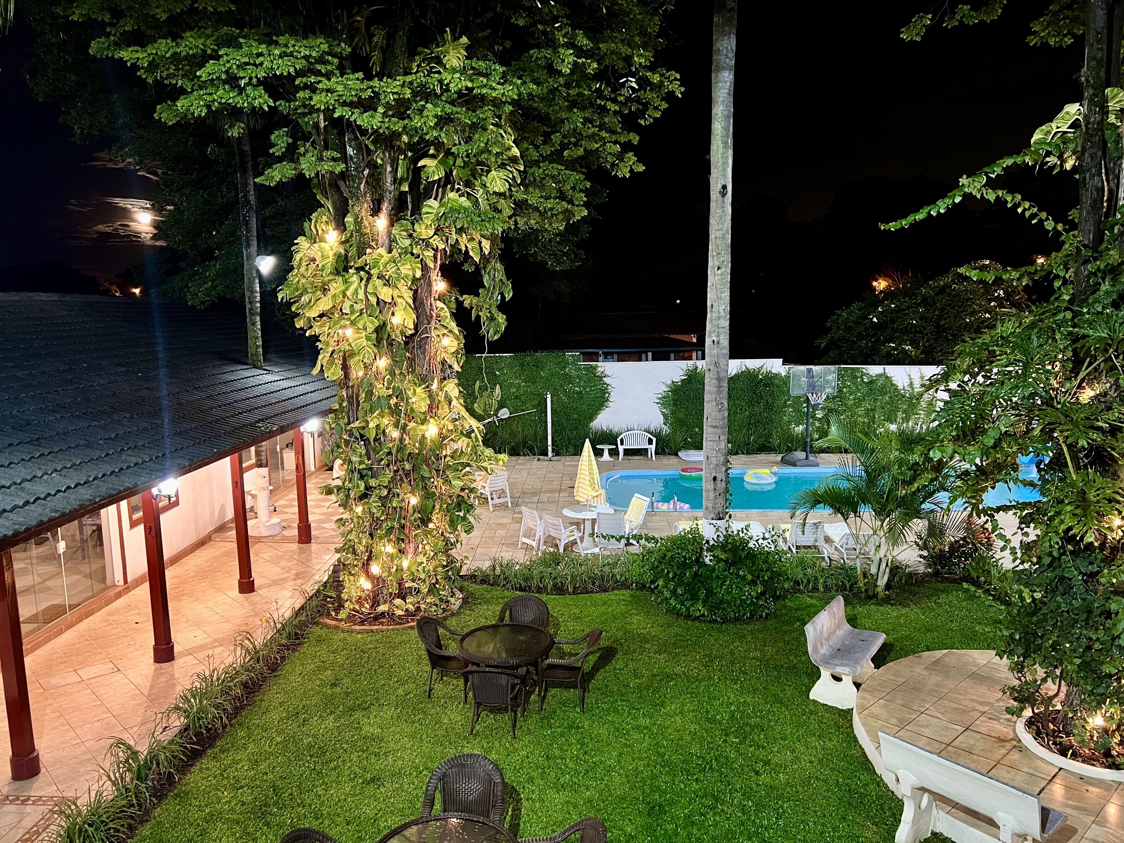 Un espacio exterior bien iluminado con piscina, sillas de descanso y una zona de estar cubierta.