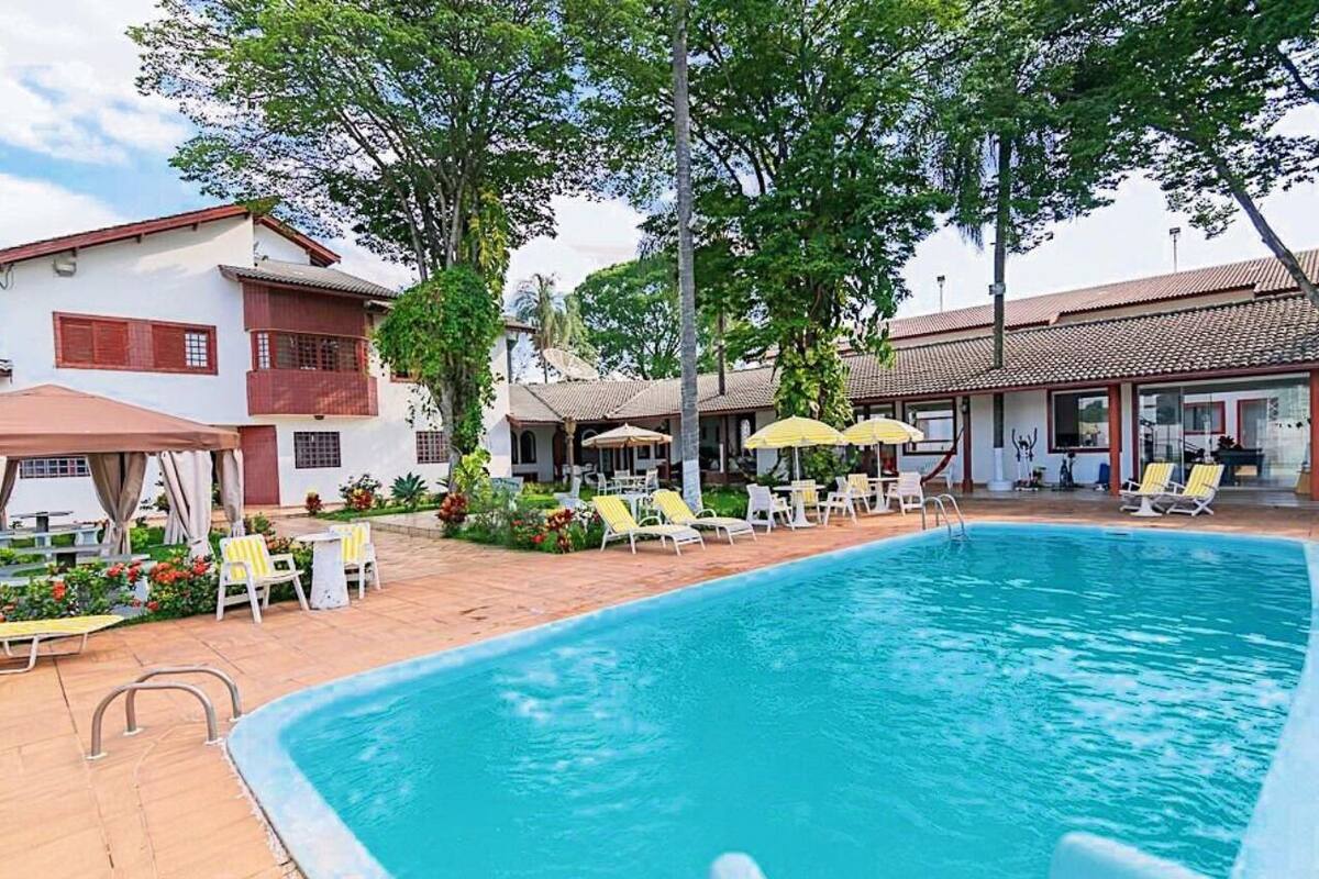 A swimming pool with lounge chairs and umbrellas, surrounded by buildings with red window frames and a tiled roof.