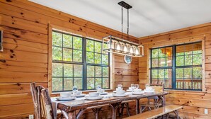 A wooden cabin dining area with a long table set for four, large windows, and a hanging light fixture. -  Dollywood - Best Location & Value (Sevierville)