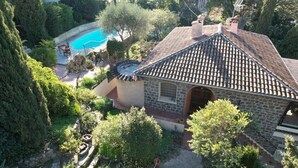 Ein Haus aus Stein mit einem Ziegeldach, einem Swimmingpool und umgebender Bepflanzung.