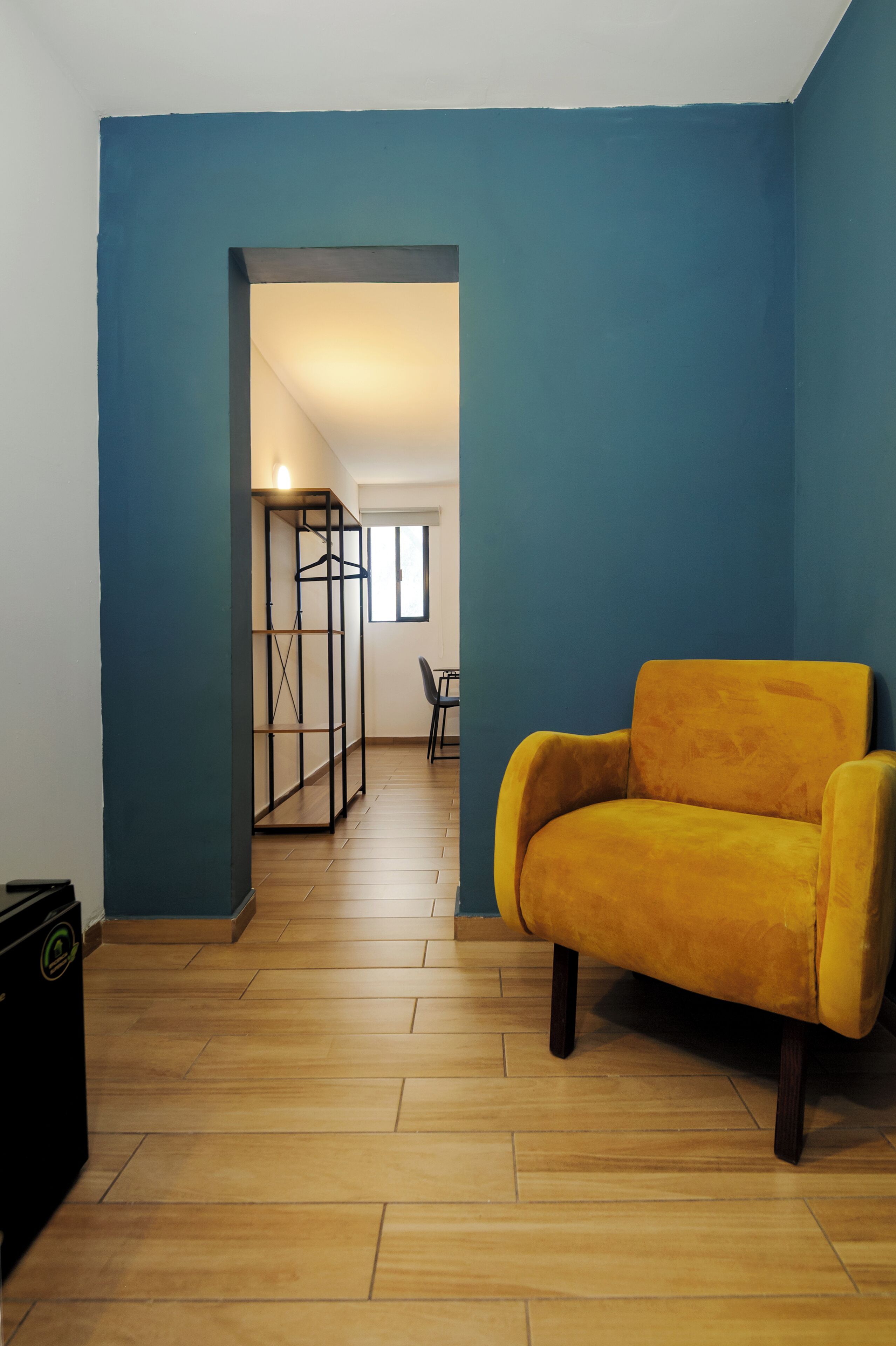 Ein Zimmer mit blauer Wand, gelbem Sessel, Holzboden und einer Kleiderstange.