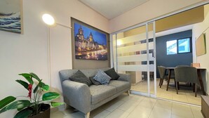 Una sala moderna con un sofá gris, una planta en maceta y un cuadro de un paisaje urbano en la pared.