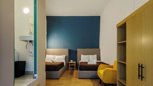 Una habitación de hotel con dos camas, una mesita pequeña, una silla amarilla y un armario.