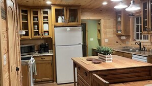 Cucina con rivestimenti in legno, isola centrale, elettrodomestici integrati e luci a sospensione.