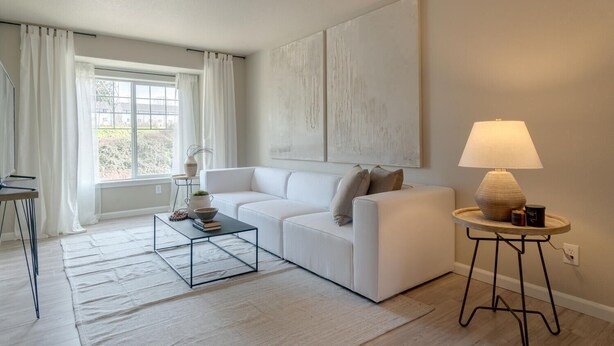 Una sala de estar moderna con un sofá blanco, una mesa de centro, una lámpara y un cuadro abstracto grande en la pared.