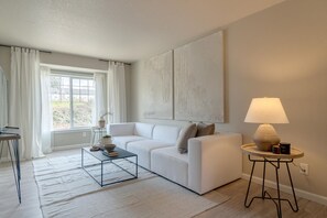 Ein modernes Wohnzimmer mit einem weißen Sofa, einem Couchtisch, einer Lampe und einem großen abstrakten Gemälde an der Wand.