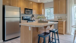 Una cocina moderna con armarios de madera, un refrigerador de acero inoxidable, un microondas, una estufa y una isla grande con taburetes de bar.