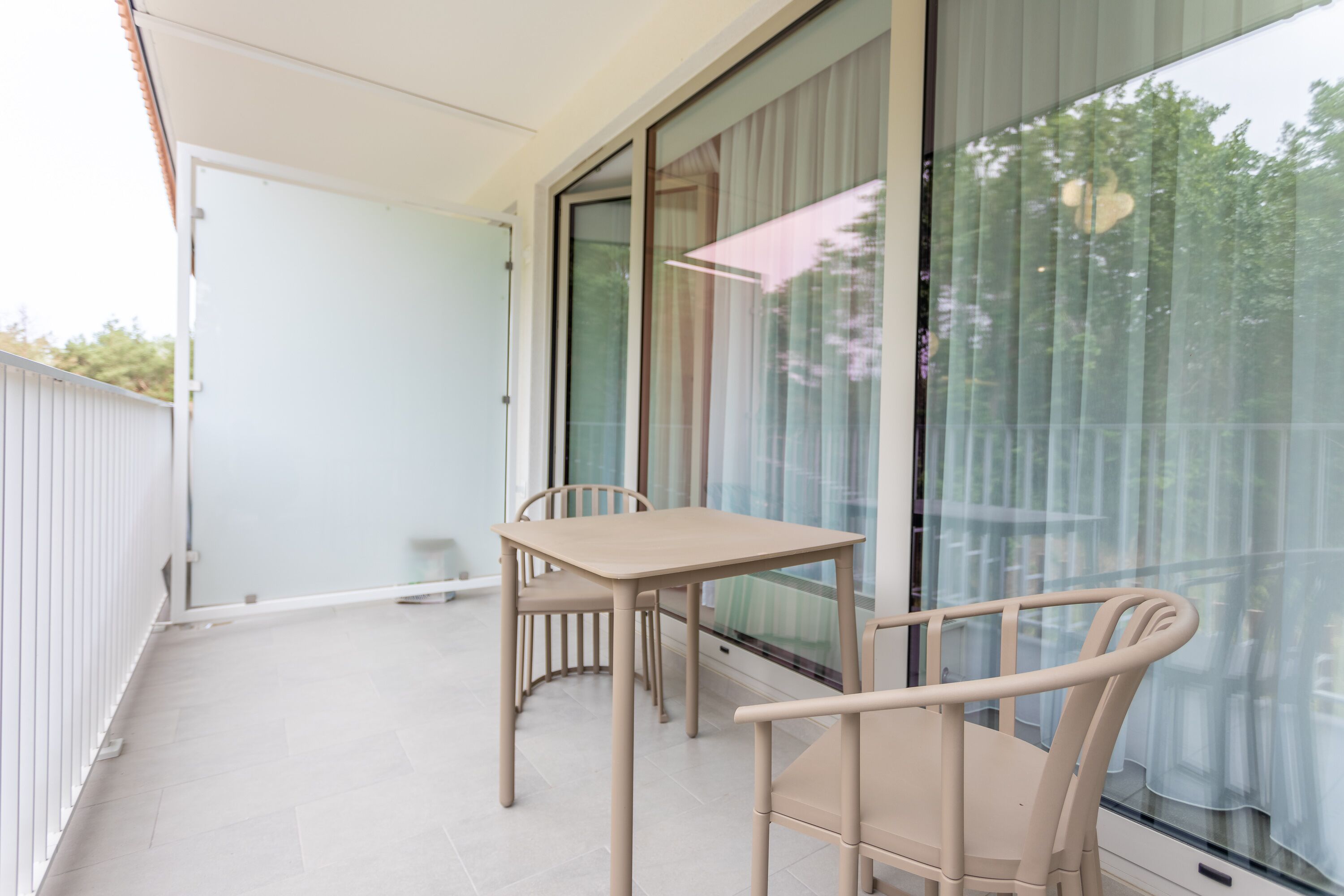 Ein Balkon mit Tisch und zwei Stühlen, große Fenster mit Vorhängen und ein weißes Geländer.