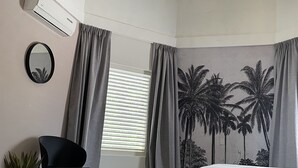 Ein Schlafzimmer mit einem Bett, einem Sessel, einer Topfpflanze, einer Wand-Klimaanlage und einer Deckenleuchte.
