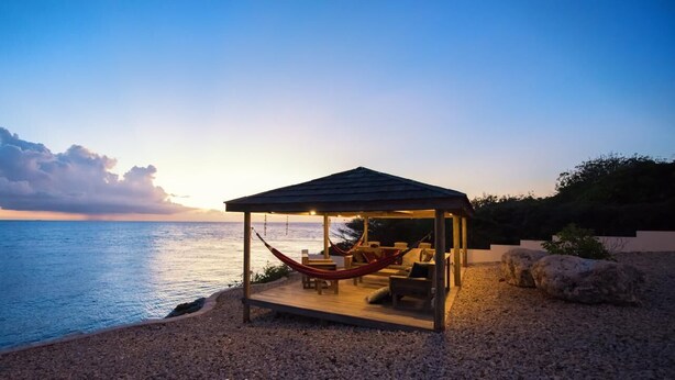 Ein Gazebo am Strand mit einer Hängematte, einer Sitzecke und Blick auf das Meer.