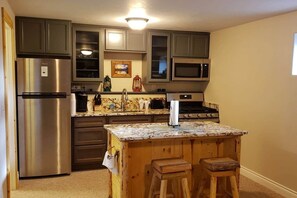 Una cocina con un refrigerador de acero inoxidable, un microondas, una estufa, taburetes de madera y una encimera de mármol.