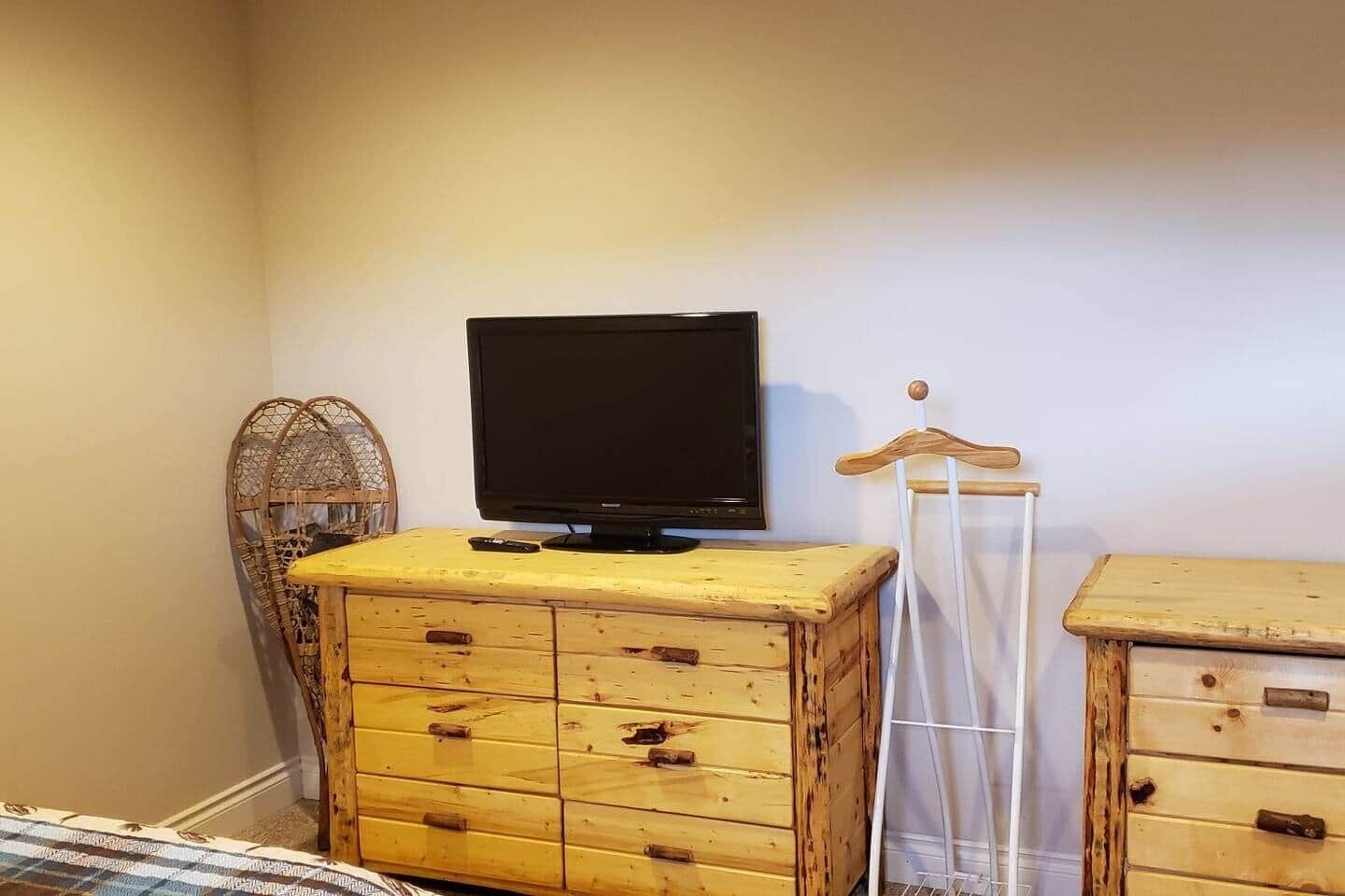 Ein Zimmer mit Fernseher auf einer Holzkommode, einem Korbsessel und einem Holzschrank.