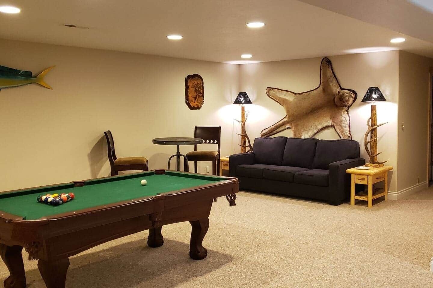 Una mesa de billar con bolas, un sofá, dos sillones y un gran tapiz de piel en la pared.