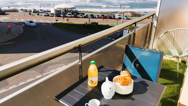 Un balcon avec une table préparée pour le petit-déjeuner, d’où l’on peut admirer un parking et l’océan.