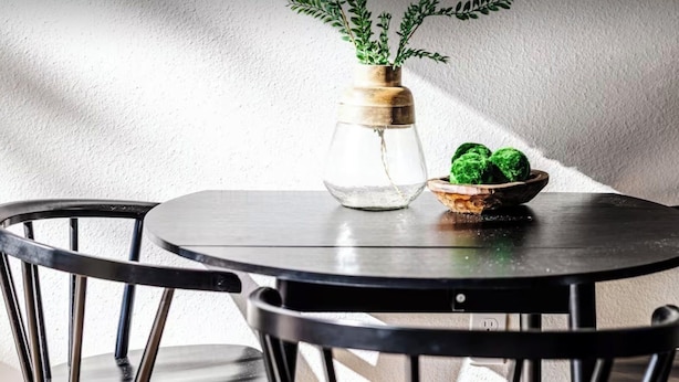 A round table with a clear vase and a bowl of green balls, accompanied by two chairs.