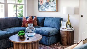 A modern living room with a blue sofa, a round wooden coffee table, and a decorative lamp.
