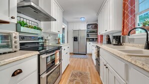 A modern kitchen with white cabinets, stainless steel appliances, a built-in oven, and a microwave. - Orion's Retreat a charming cottage nestled by the scenic shores of Lake Sinclair (Eatonton)