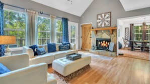 A spacious living room with a fireplace, large windows, and a ceiling fan. - Orion's Retreat a charming cottage nestled by the scenic shores of Lake Sinclair (Eatonton)