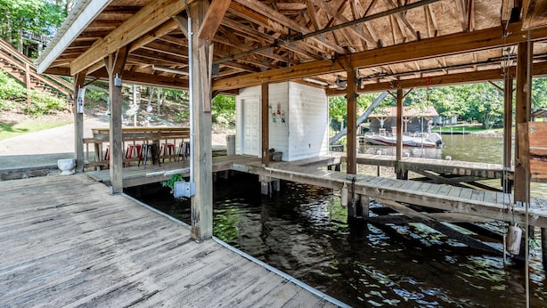 A wooden dock extending over water, supported by beams and columns, with a covered seating area and a white building nearby. - Orion's Retreat a charming cottage nestled by the scenic shores of Lake Sinclair (Eatonton)