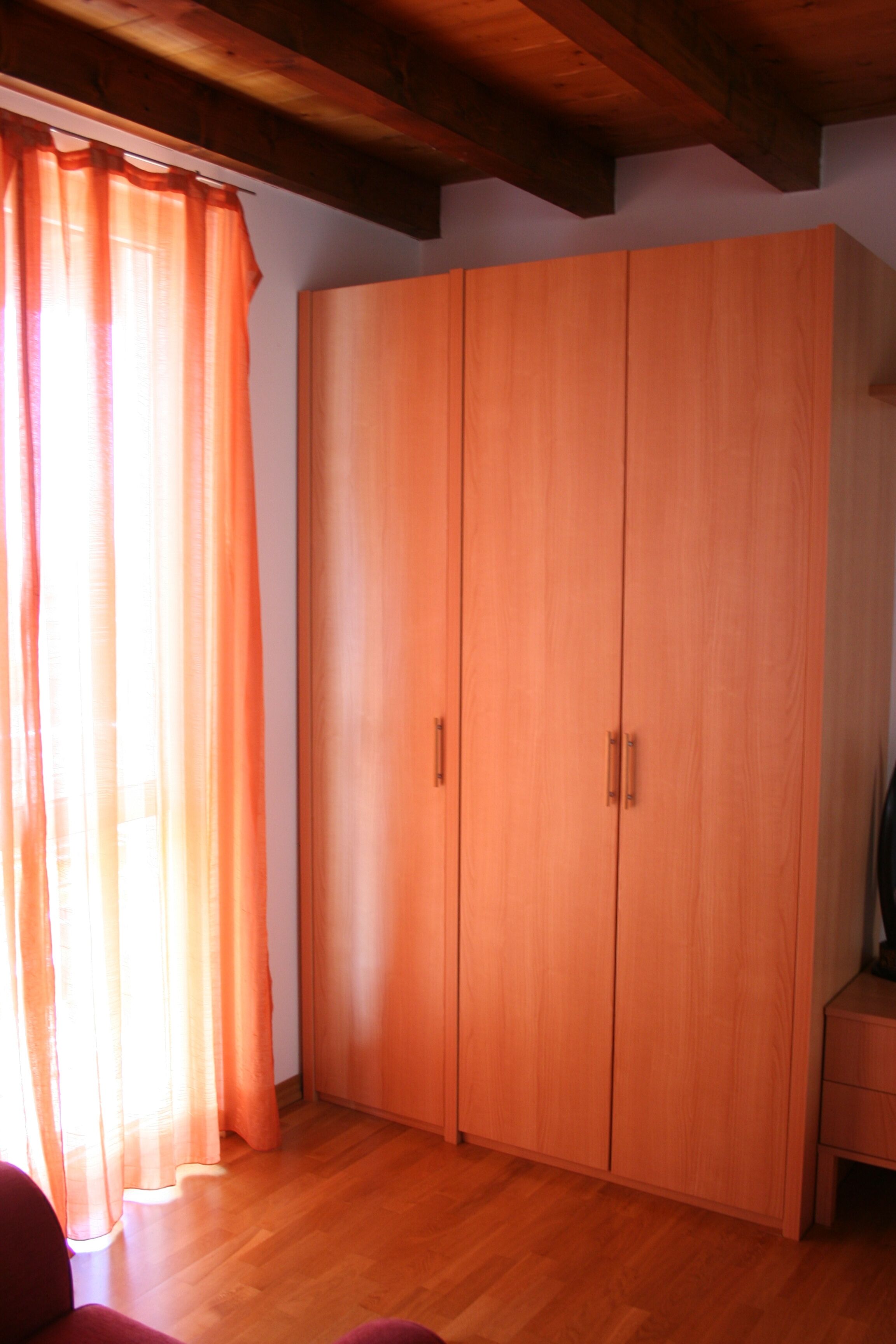 Habitació amb un armari de fusta, terra de fusta i una finestra amb cortines taronja.