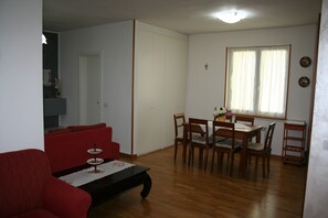 A living room with a red sofa, a wooden dining table with chairs, and a small table with a vase of flowers. - Sophie's Tavern 4 km from spas - CIN: IT052026C2ORC66IOV (Serre di Rapolano)