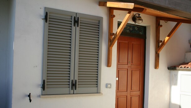Un bâtiment doté d’une porte et de volets en bois, d’une petite fenêtre et d’un luminaire placé au-dessus de la porte.
