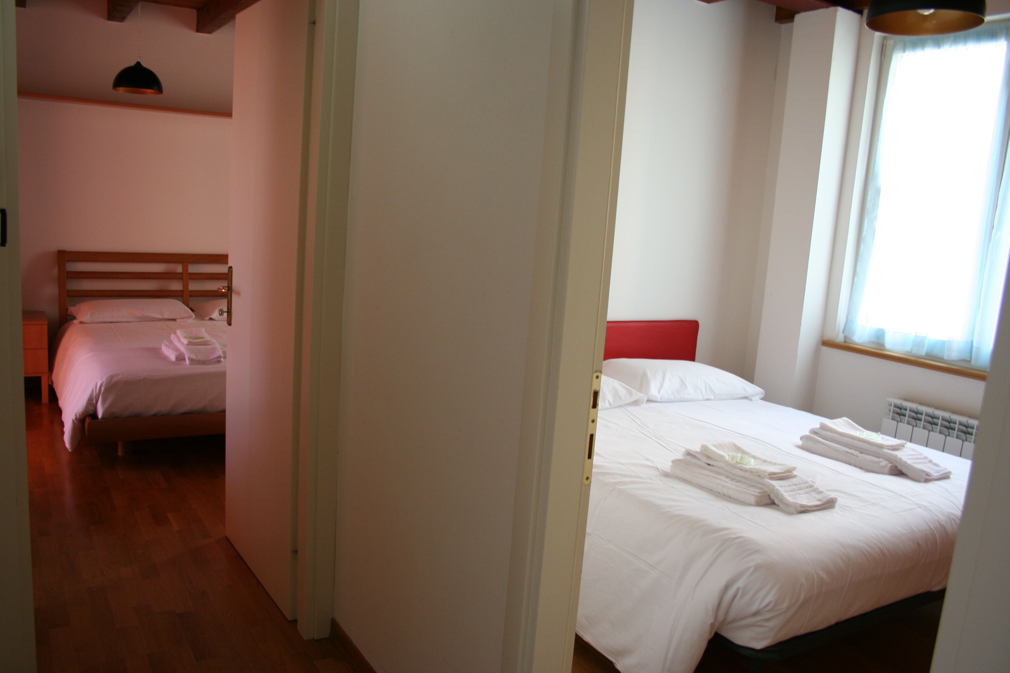A hotel room with a wooden bed frame, a red headboard, and a window with curtains.