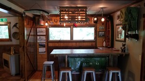 A rustic bar area with wooden walls, a green bar counter, and three metal stools. - A Cabin in Rochford (Hill City)