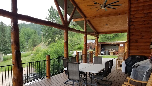 A wooden deck with a table and chairs, a grill, and a view of a forested area. - A Cabin in Rochford (Hill City)