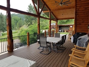 Una terraza techada al aire libre con mesa y sillas, una parrilla y vistas a un área boscosa.