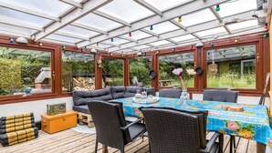 Eine überdachte Terrasse mit Esstisch, umgeben von Korbstühlen und einer Couch.