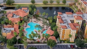 A hotel with a central swimming pool surrounded by palm trees and a parking lot. - Designer 3BR/2BA Corner Suite - Disney & Universal (Orlando)